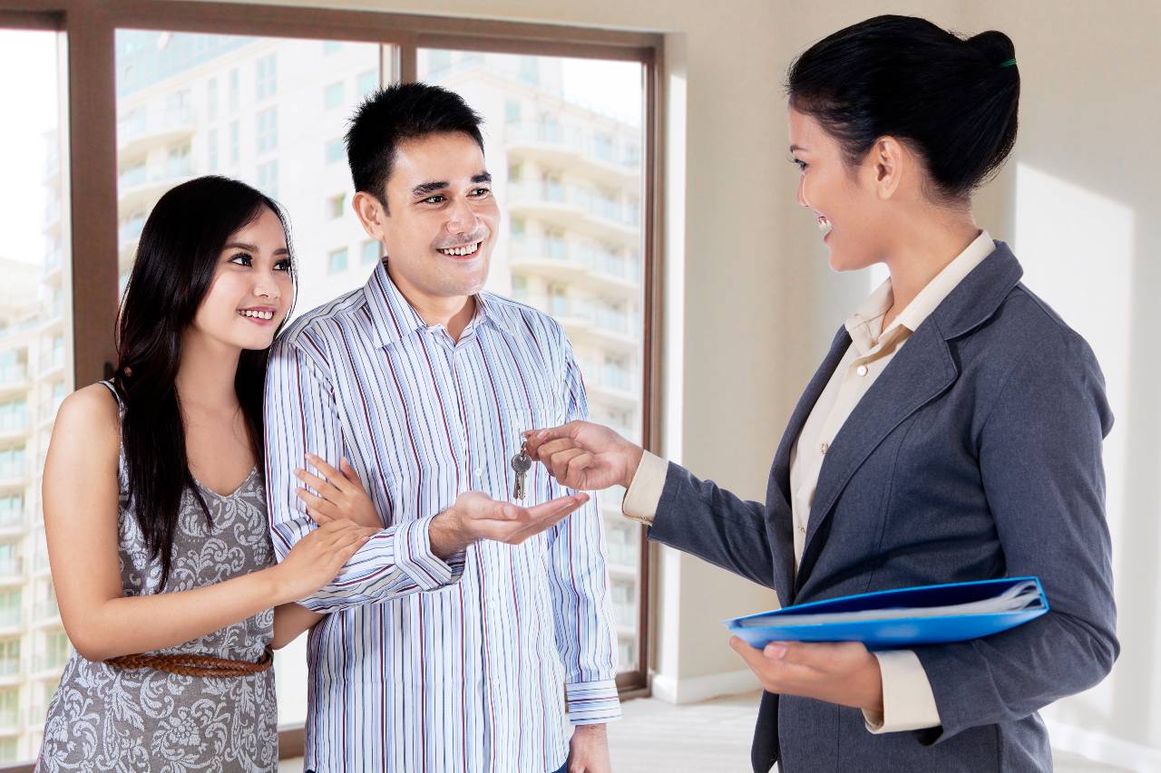 Real estate agent handing over keys of new house to young couple